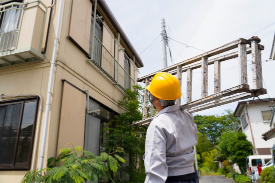 大きな脚立を肩に担いで運搬する作業員